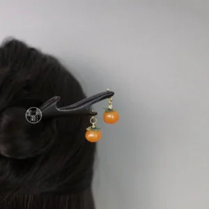 Persimmon-themed traditional Chinese hair stick shown in a coiled bun hairstyle, featuring a dark wooden antler-inspired pin body, orange fruit pendants, and gold-tone hanging hardware