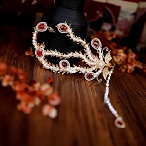 Top-down view of an ornate phoenix-shaped Chinese hair pin with gilded filigree, red crystal accents, imitation pearls, and a long pearl tassel on a dark wooden table