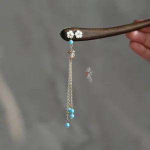 Close-up of a traditional Chinese wooden hair stick with white floral ornament, blue beaded golden tassel, and dark brown shaft for Hanfu hairstyles