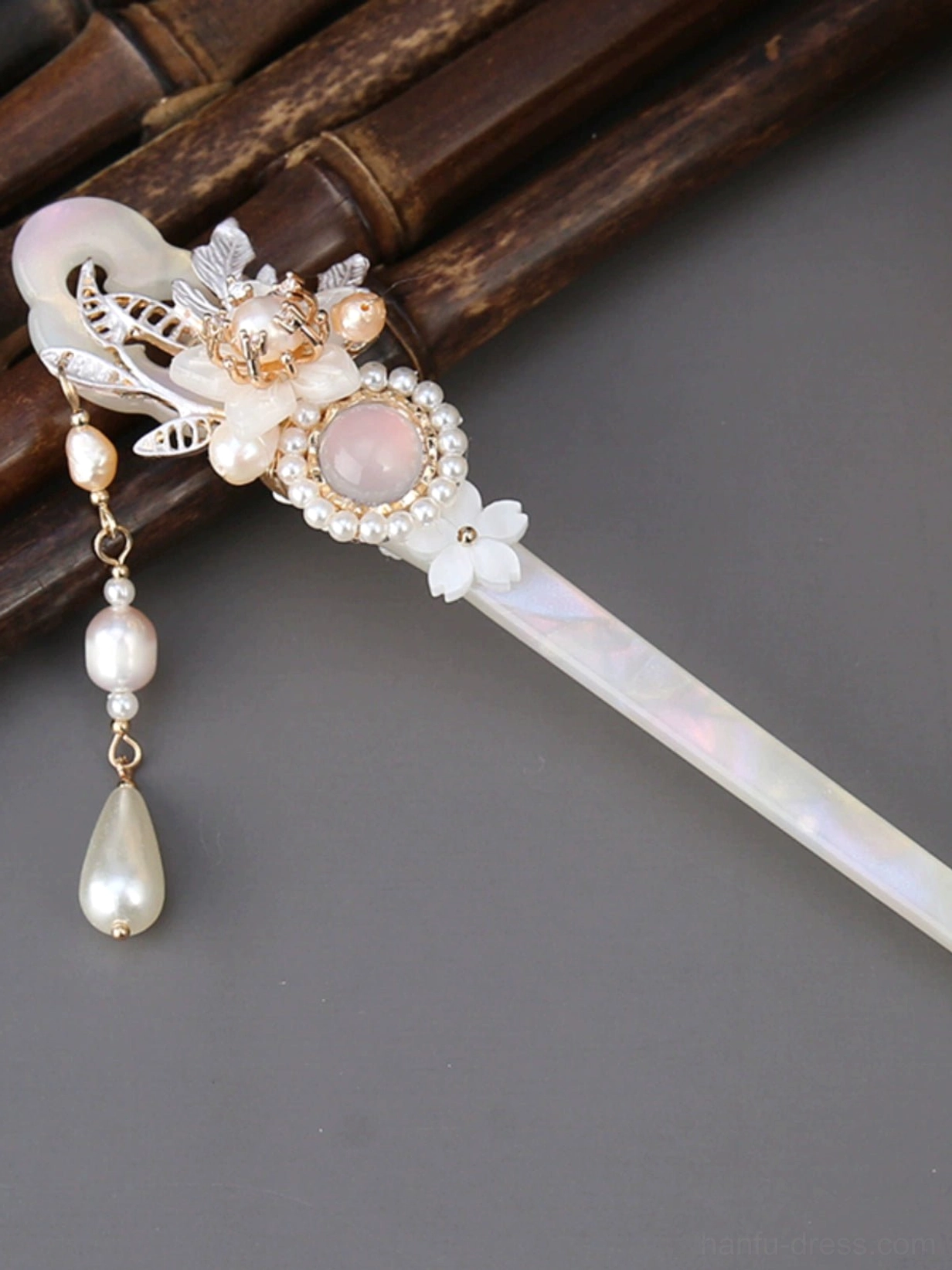 Ancient Chinese style hair stick with gold floral ornament, pink center gem, pearl clusters, and dangling tassel displayed on a bamboo mat