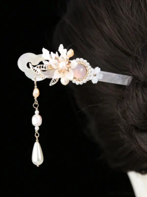 Traditional Chinese hair stick with iridescent shaft, pink floral gem, white shell flowers, and pearl teardrop tassel secured in a dark hair bun