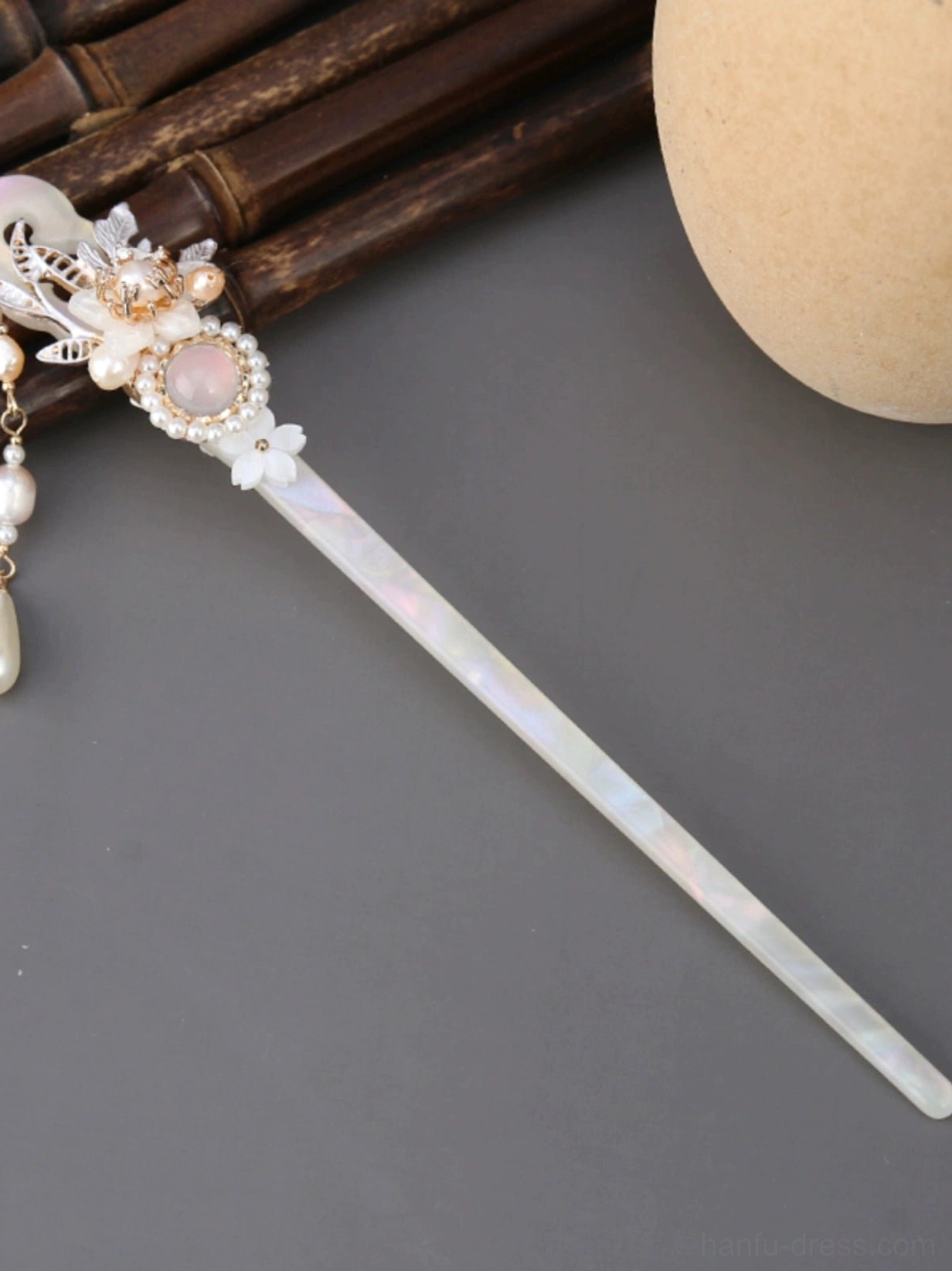 Side view of a traditional Chinese tassel hair stick showing the iridescent shaft, pink floral ornament, and dangling pearl pendant