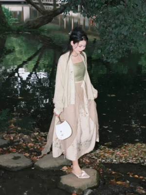 Rear side view of a pine green modern Hanfu dress set with Song-style cardigan worn beside a tranquil waterside garden with autumn leaves