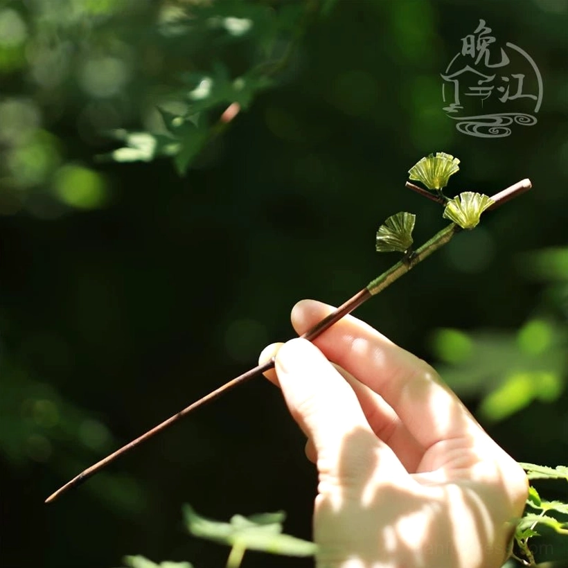 Handheld pine needle Chinese hair stick with three translucent green woodland ornaments and a slender tapered dark brown wooden shaft