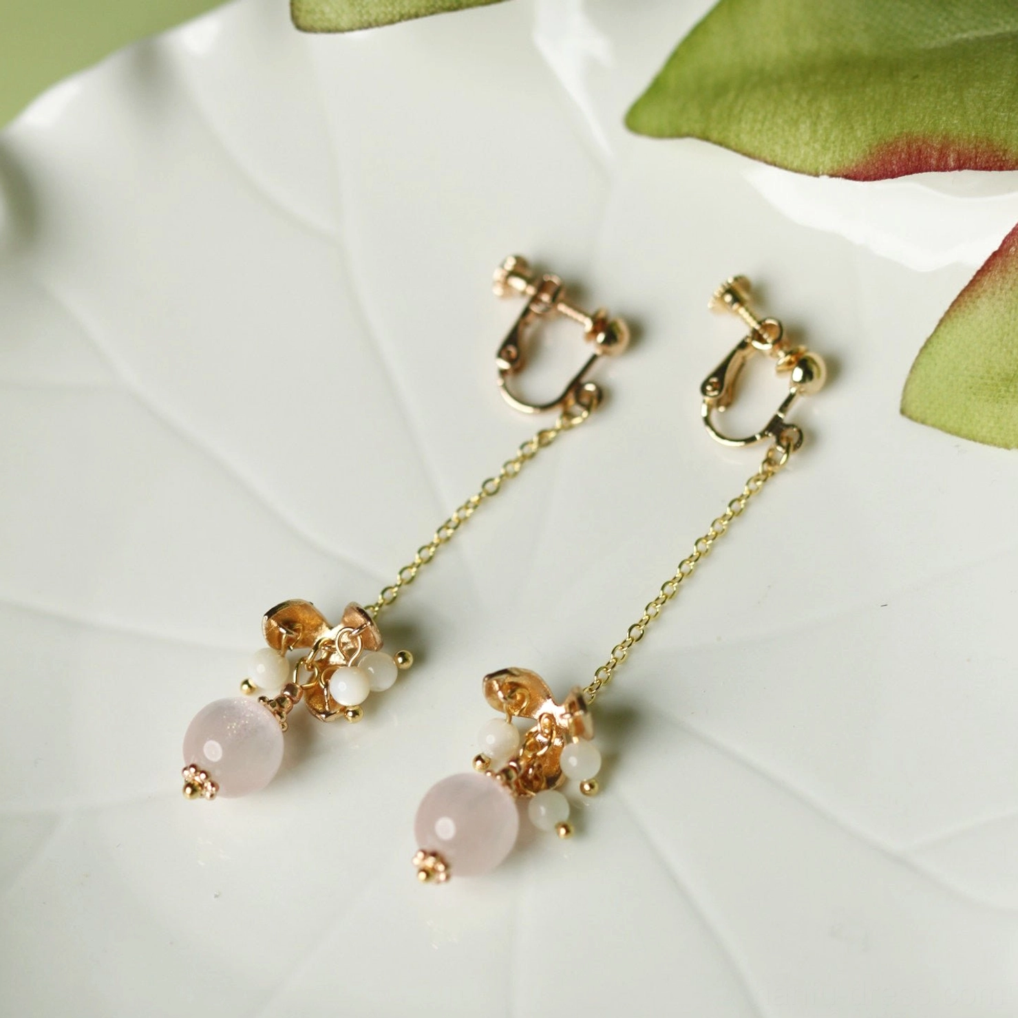 Non-pierced pink beaded long dangle Chinese Hanfu comfort clip-on earrings displayed on a white leaf-pattern ceramic plate