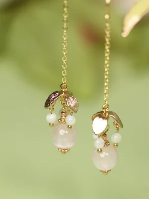 Close-up of pink beaded long dangle Chinese earrings with gold tone hardware, pearl white bead clusters, and delicate chain tassels