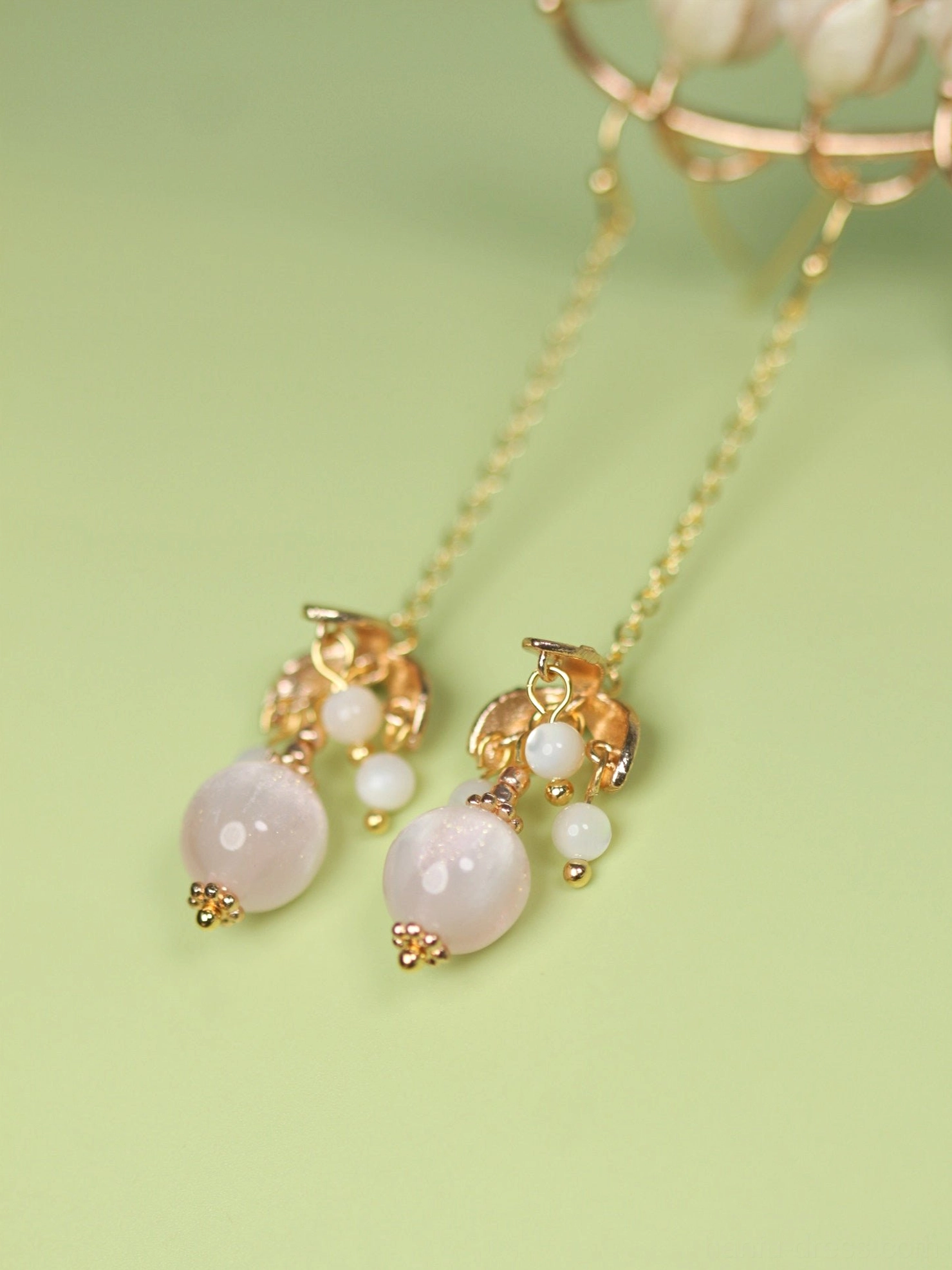 Pair of pink and white beaded long dangle Chinese earrings in gold tone metal shown flat lay on a light green background