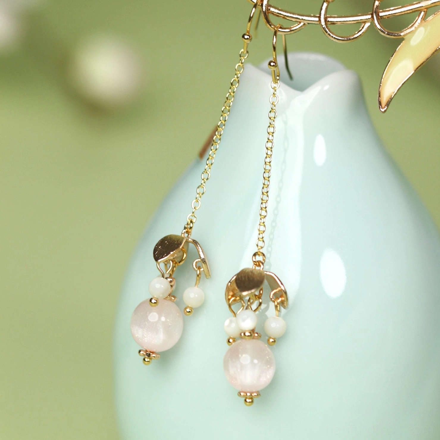 Pink beaded long dangle Chinese Hanfu hook earrings hanging from a light cyan ceramic vase with gold tone chain drops