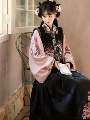 Side view of a woman seated in a pink and black modern Hanfu outfit with floral sleeves, layered vest, and Chinese-inspired horse-face skirt
