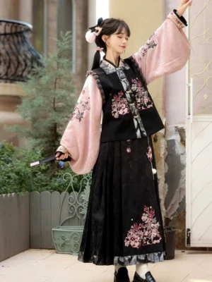 Front high-angle view of a woman wearing a pink and black modern Hanfu set with floral details, cross-collar top, embroidered vest, and mamianqun horse-face skirt