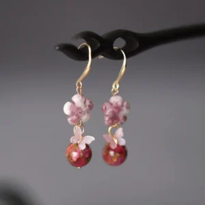 Pink blossom and burgundy marbled bead Chinese dangle earrings with gold hook ear wires displayed on a black wooden hairpin