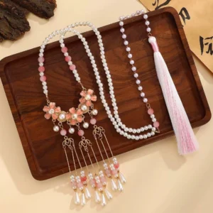 Pink blossom Yingluo Chinese necklace with pearl bead chains, drop pearl tassels, and gradient pink white silk tassel displayed on a dark wooden tray with Chinese calligraphy