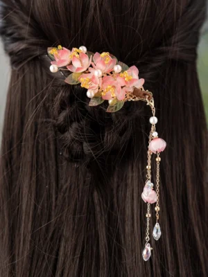 Close-up of a pink floral Hanfu hair clip worn in braided dark hair with pearl decorations, gold chains, pink beads, and long clear crystal tassels