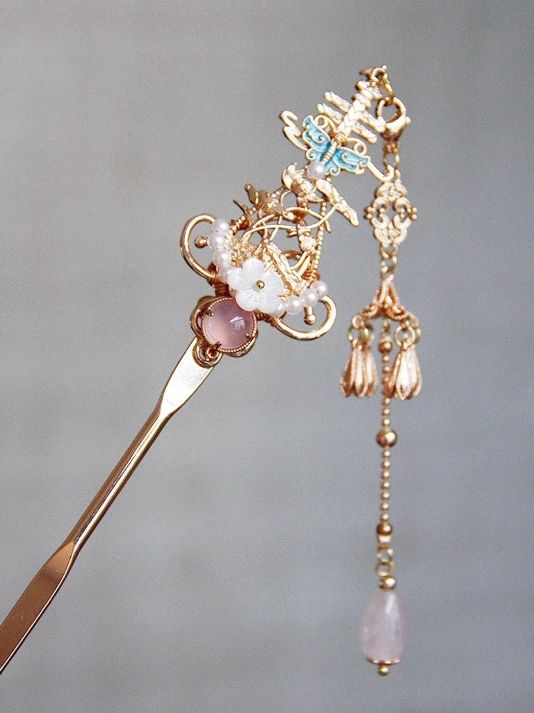 Close-up of a pink Chinese hair stick with pink gemstone inlay, white shell flower, blue enamel butterfly and layered pink tassel pendant