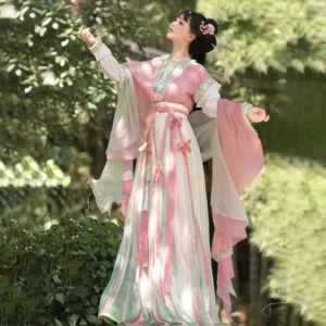 Pink and cream Tang Dynasty Hanfu Beizi Qiyao Ruqun outfit shown in a bamboo forest, with flowing pink outer panels, a striped long skirt, floral hair accessories, and a tassel waist sash