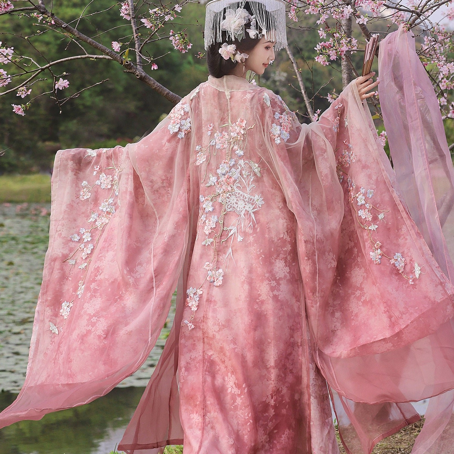 Back view of pink fairy Hanfu costume with embroidered wide-sleeve robe, sheer fabric, and matching floral fringe hair crown