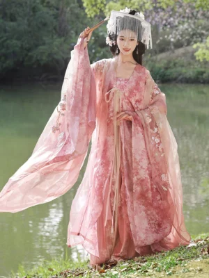 Pink fairy Hanfu set with flowing wide sleeves, floral details, waist ribbon, and traditional Chinese styling in a lakeside outdoor setting