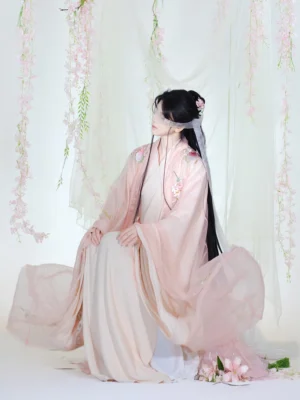 Side three-quarter view of a pink floral embroidered Chinese fantasy hanfu costume with layered sheer robe, flowing skirt, wide sleeves, and elegant kneeling pose