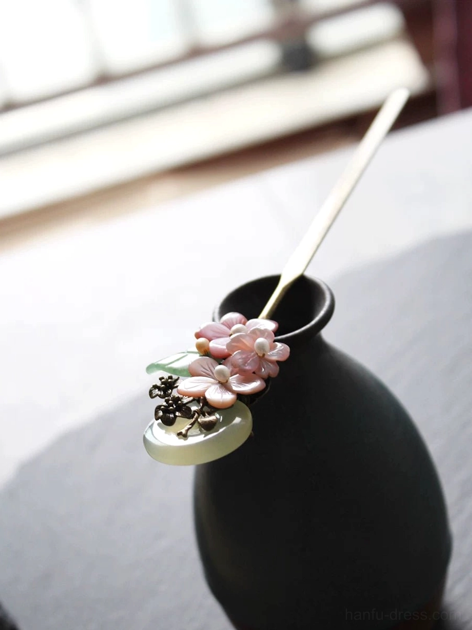Traditional Chinese Hanfu hair stick displayed in ceramic vase, featuring pink flower clusters, green leaf accents, round jade-look moon charm, and bronze metalwork