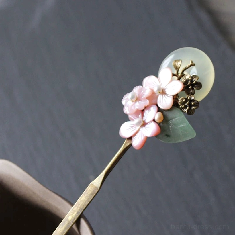 Close-up of pink floral full moon Chinese hair stick for Hanfu, featuring shell-like blossoms, jade-inspired pendant, green leaves, bronze ornaments, and brass pin