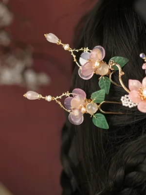 Pink floral Hanfu hair pin styled in dark braided hair with translucent flower petals, green jade-style leaves, pearl accents, gold-tone metal, and a delicate hanging tassel