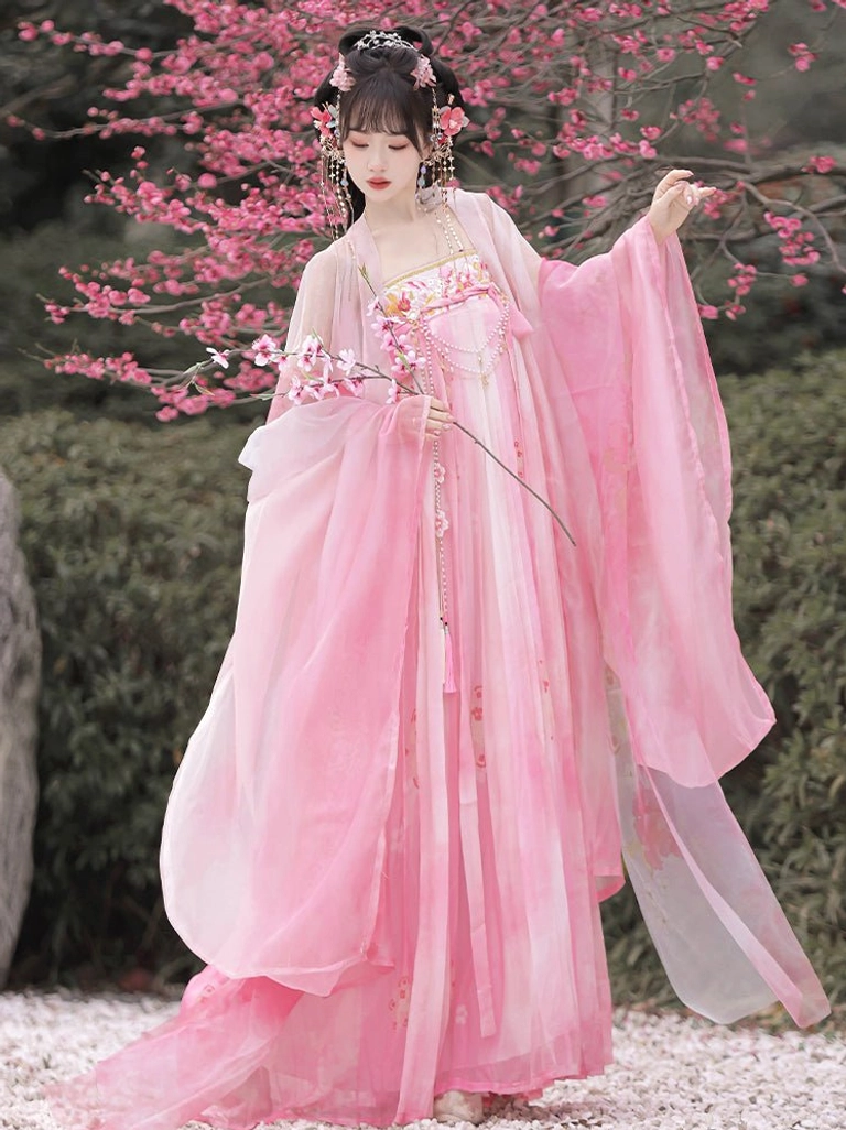 Pink Tang Dynasty Qixiong Ruqun Hanfu with peach blossom prints, long flowing skirt, and wide sleeves beside flowering branches