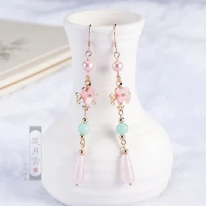 Pink flower goddess Hanfu earrings with mint green beads and gold details displayed on a white porcelain vase