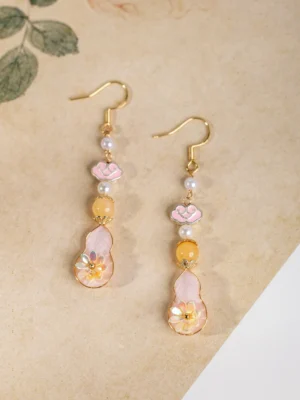 Front flat lay of pink gourd Chinese earrings featuring gold hooks, layered pearl and yellow bead strands, pink cloud charms, and flower-patterned gourd drops