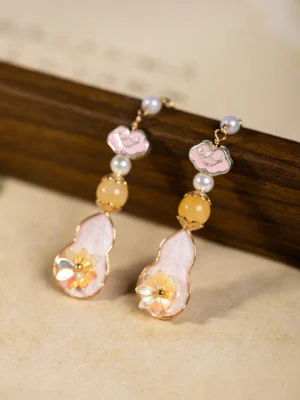 Pink gourd Chinese Hanfu drop earrings with pink cloud charms, white pearl beads, yellow accents, floral gourd pendants, and gold hook closures on a vintage background
