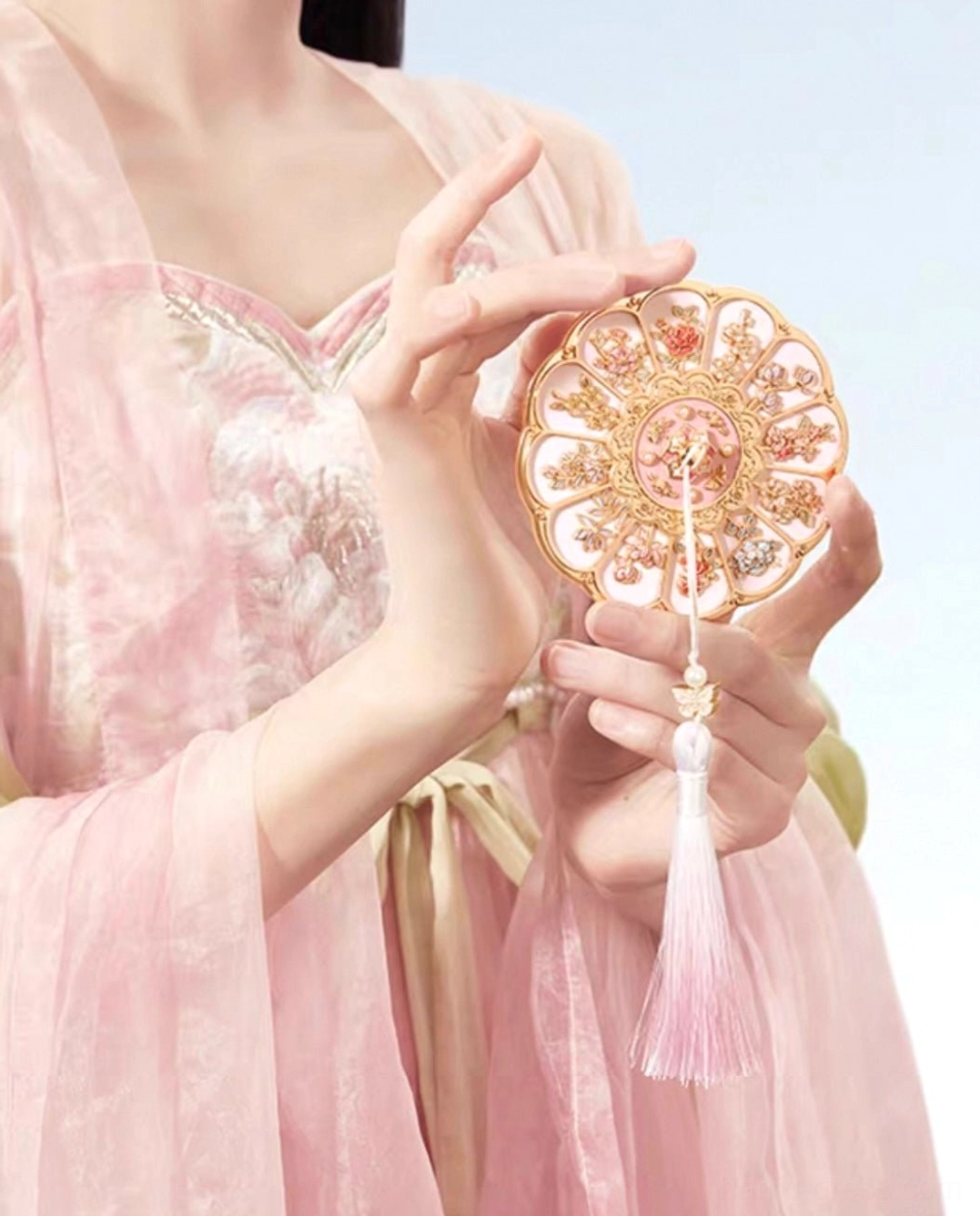 Close-up of a woman in pink Hanfu holding a decorative Chinese pocket mirror with a flowing pink tassel