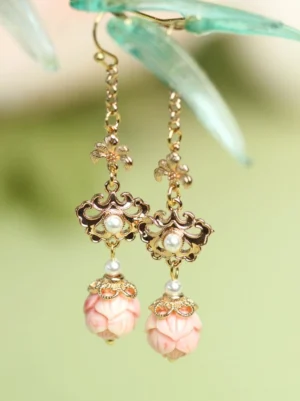 Pink lotus bud Chinese earrings with vintage gold openwork floral details and white pearl accents displayed on a light green bamboo-inspired background