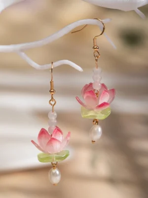 Pink lotus drop hanfu earrings with gold ear hooks, green leaf accents, white beads, and freshwater pearl pendants displayed on a decorative branch