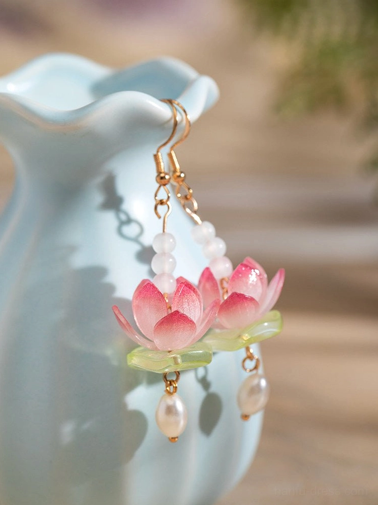 Pair of pink lotus hanfu earrings with layered beaded chains, freshwater pearl drops, and gold-toned hardware beside a blue ceramic vase