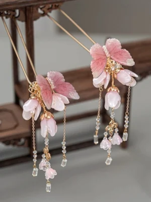 Pair of pink butterfly and magnolia Chinese hair sticks with crystal beaded tassels displayed on a vintage wooden stand