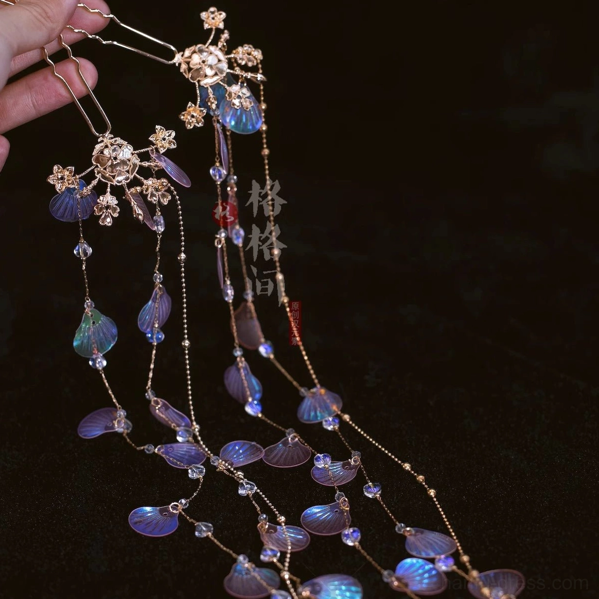 Pink and purple mermaid Hanfu hair pins with deep iridescent shell pendants gold floral tops and flowing tassel chains held against dark background
