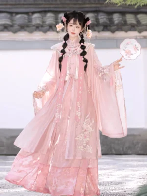 Front view of a soft pink Ming Dynasty Hanfu set with embroidered robe, wide flowing sleeves, cloud collar, and pleated mamian skirt worn in a Chinese garden