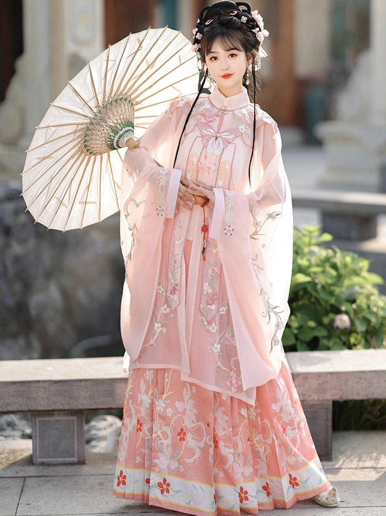 Pink Ming-style Hanfu full set with sheer embroidered blouse, matching floral mamian skirt, and decorative hem in a classical garden