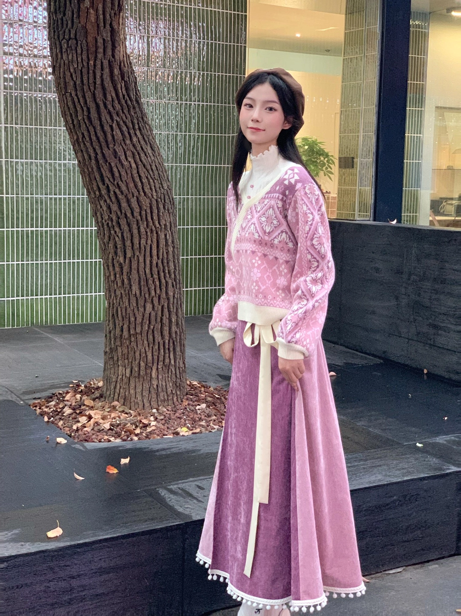 Side view of a pink Chinese-style wrap knit sweater and mauve velvet skirt outfit with cream trim in an outdoor courtyard
