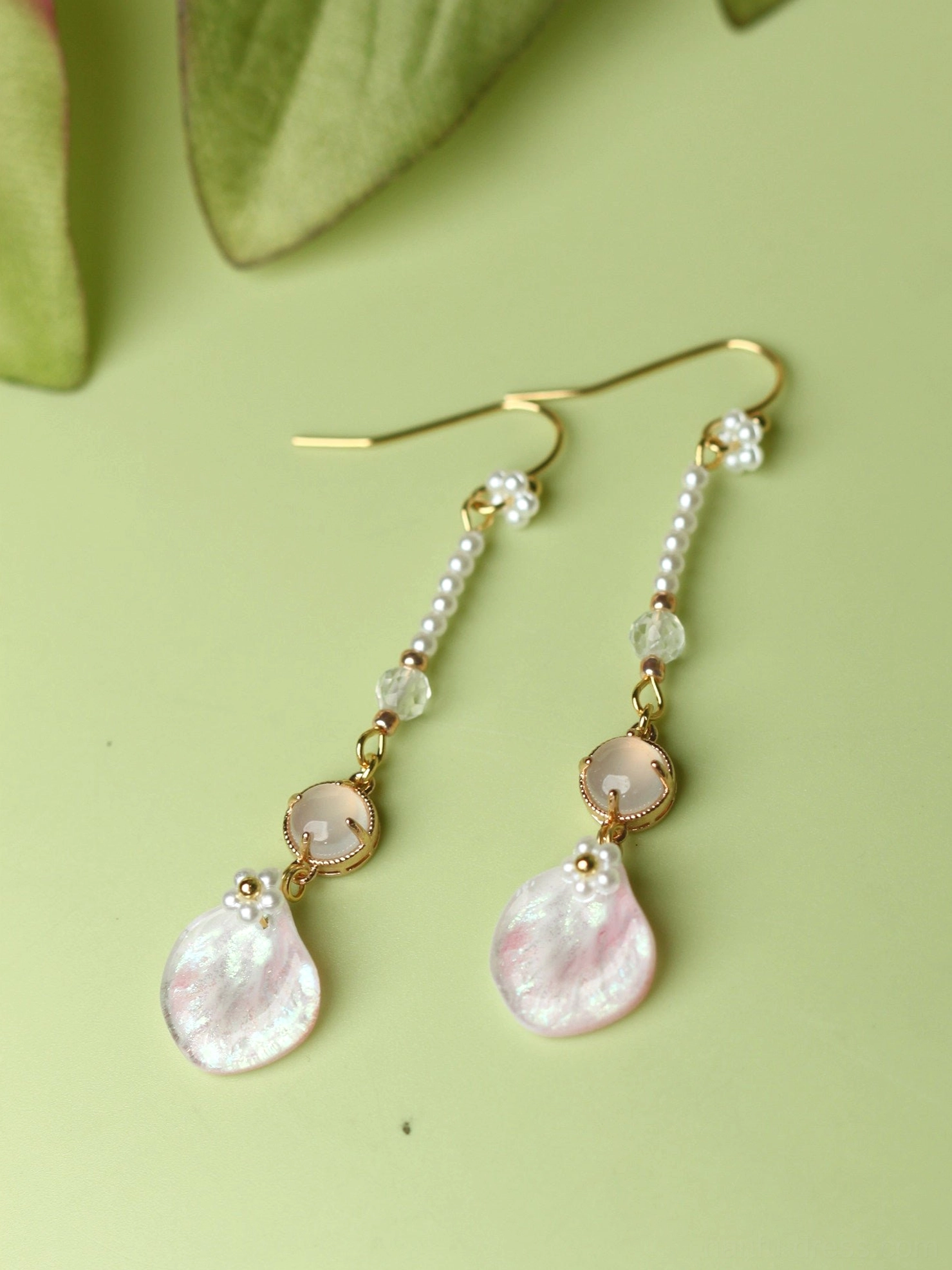 Flat lay of pink petal Chinese earrings with gold ear hooks beaded chains pink round charms and shimmering petal drops on a green background