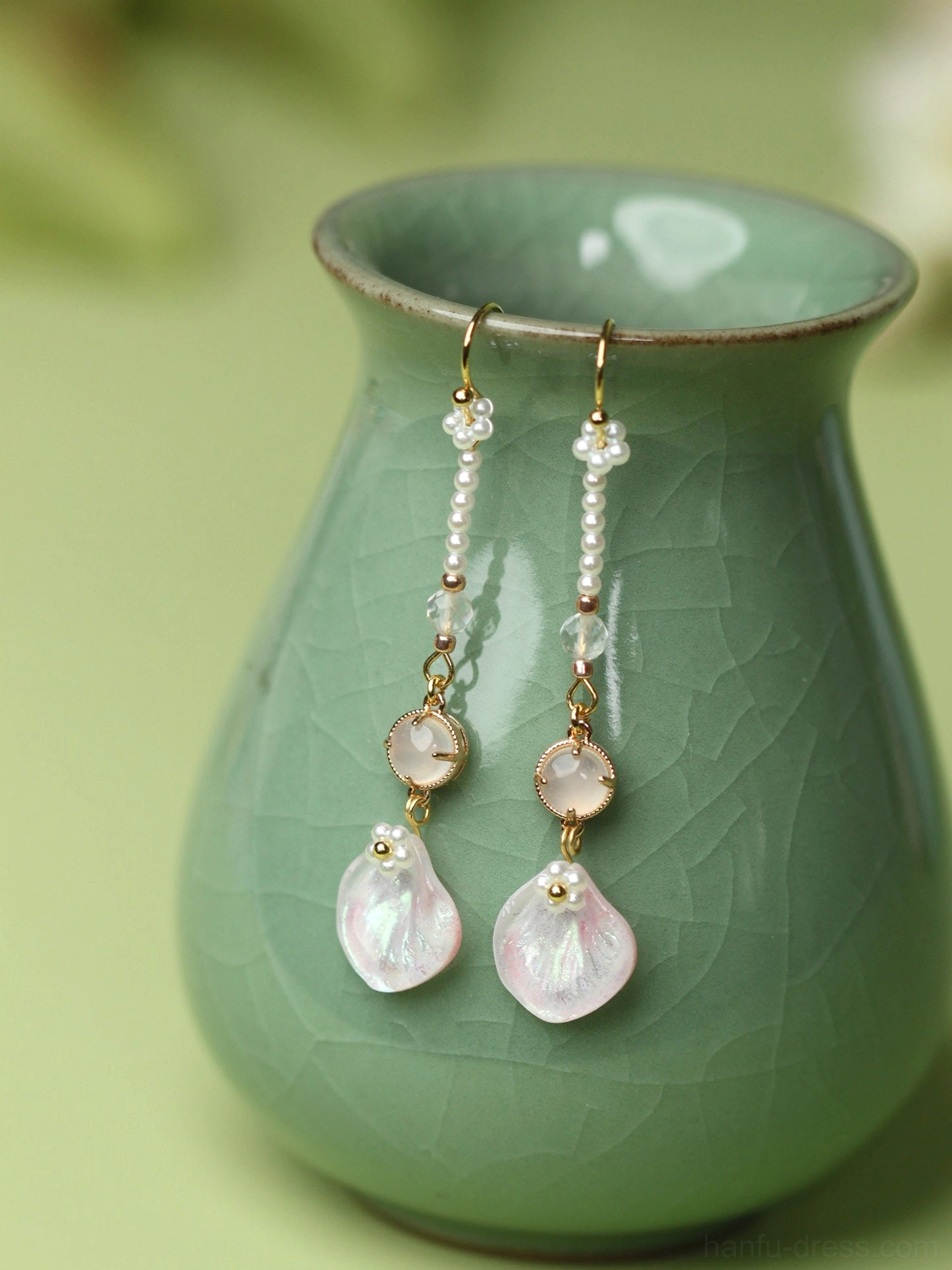 Pink petal Hanfu earrings hanging from a celadon green vase with gold hardware pearl bead chains and iridescent pink flower pendants