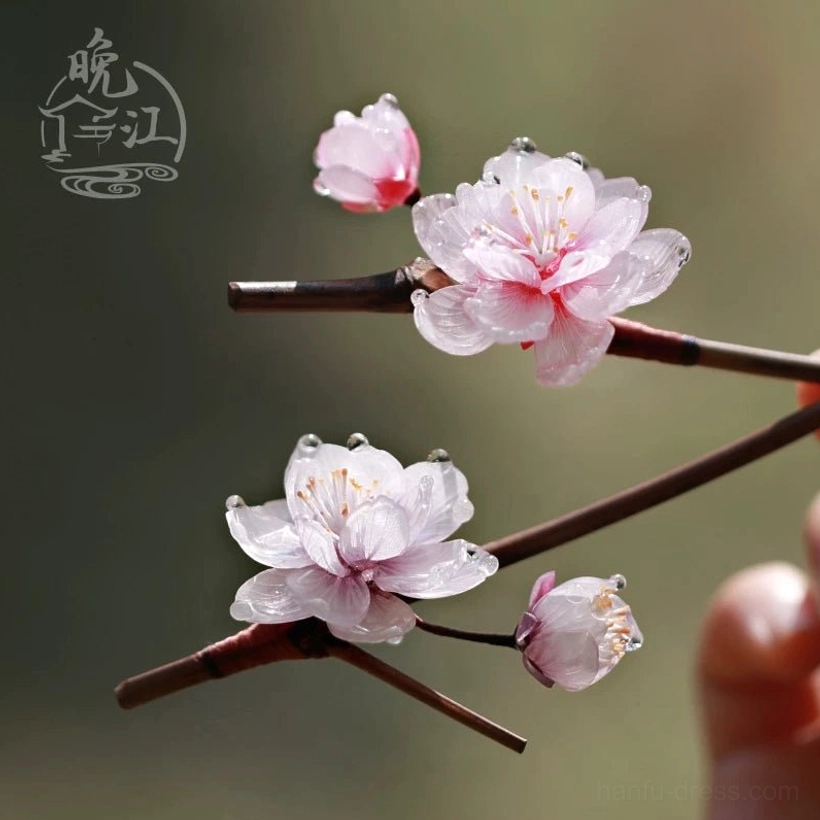 Pink plum blossom Chinese hair stick with translucent resin petals dewdrop accents and dark brown wooden shaft displayed on a decorative branch