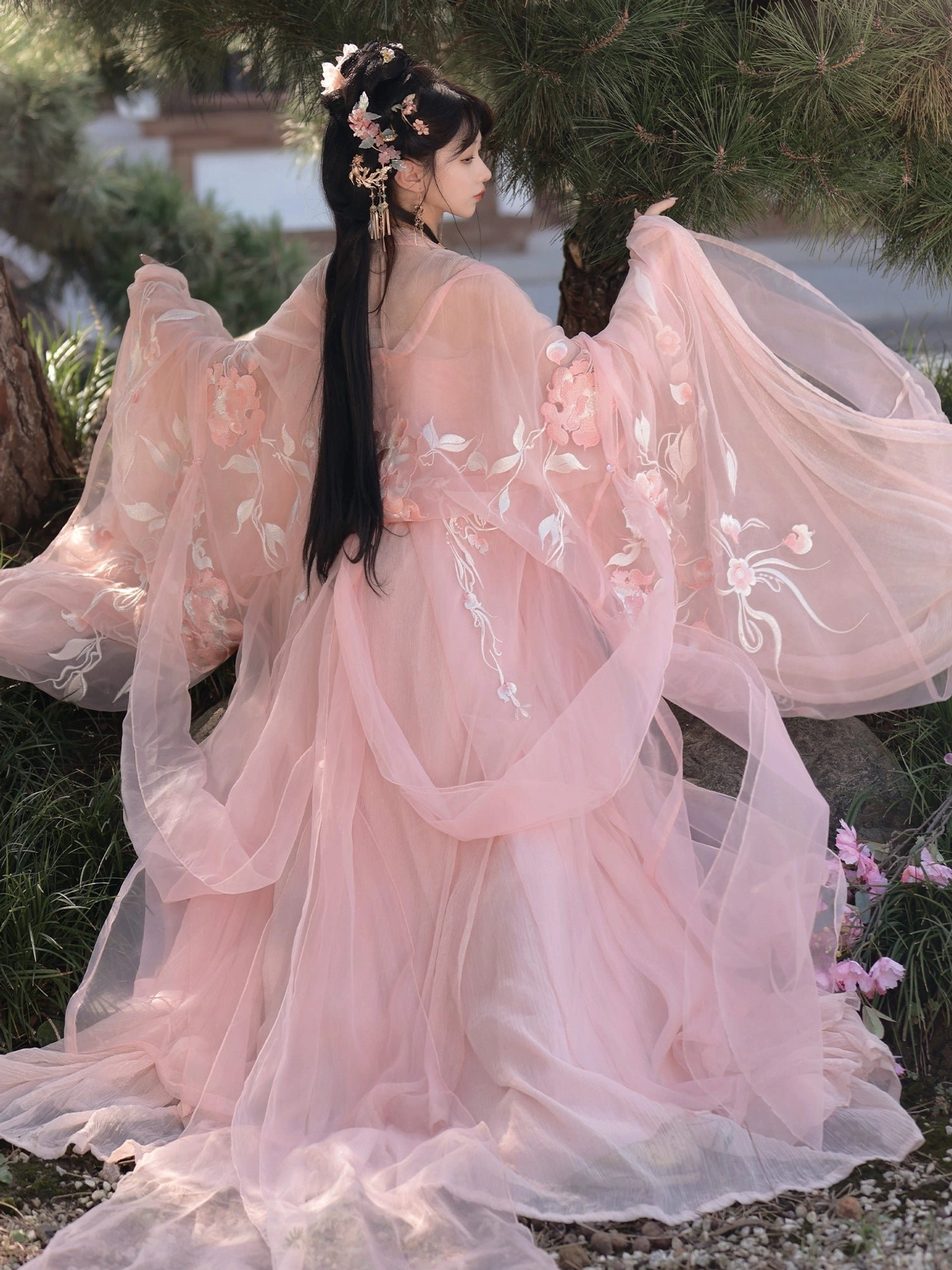Back view of pink Tang Dynasty Qixiong Ruqun hanfu with delicate floral embroidery, sheer flowing sleeves, long train, and traditional hairpins in a garden setting
