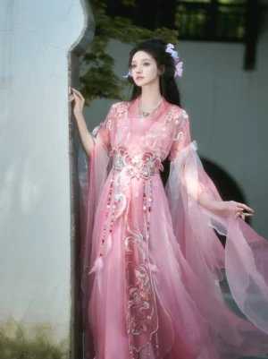 Three-quarter side view of pink Qiyao Ruqun Hanfu with phoenix embroidery, gradient organza skirt, flowing sleeves, and floral hair accessories beside a traditional white garden arch