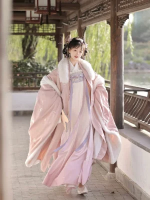 Pink Tang Dynasty Qixiong Ruqun hanfu set shown from the front with white fur-trimmed collar and sleeves, floral embroidery, wide sleeves, and a flowing floor-length skirt in a traditional Chinese garden