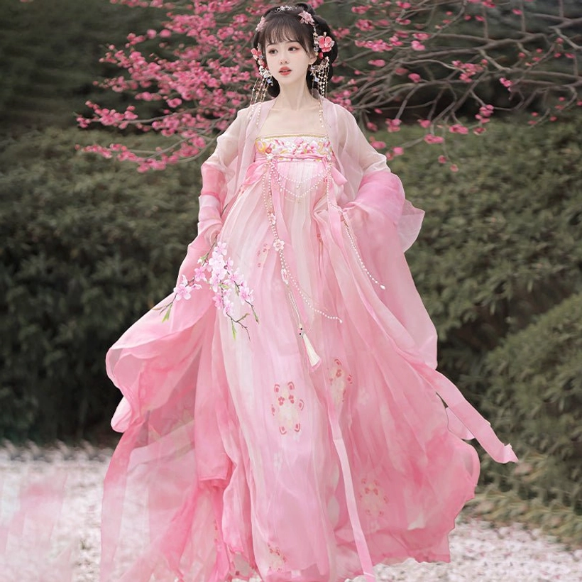 Pink Tang Dynasty Qixiong Ruqun Hanfu front view with peach blossom skirt print, tassel chest pendant, and elegant floral hair accessories