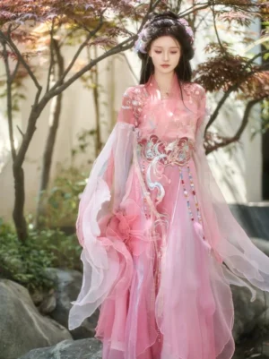 Front full-body view of a pink Wei Jin Dynasty Qiyao Ruqun Hanfu with sheer wide sleeves, embroidered waist ornament, tassel details, and flowing skirt in a classical Chinese garden