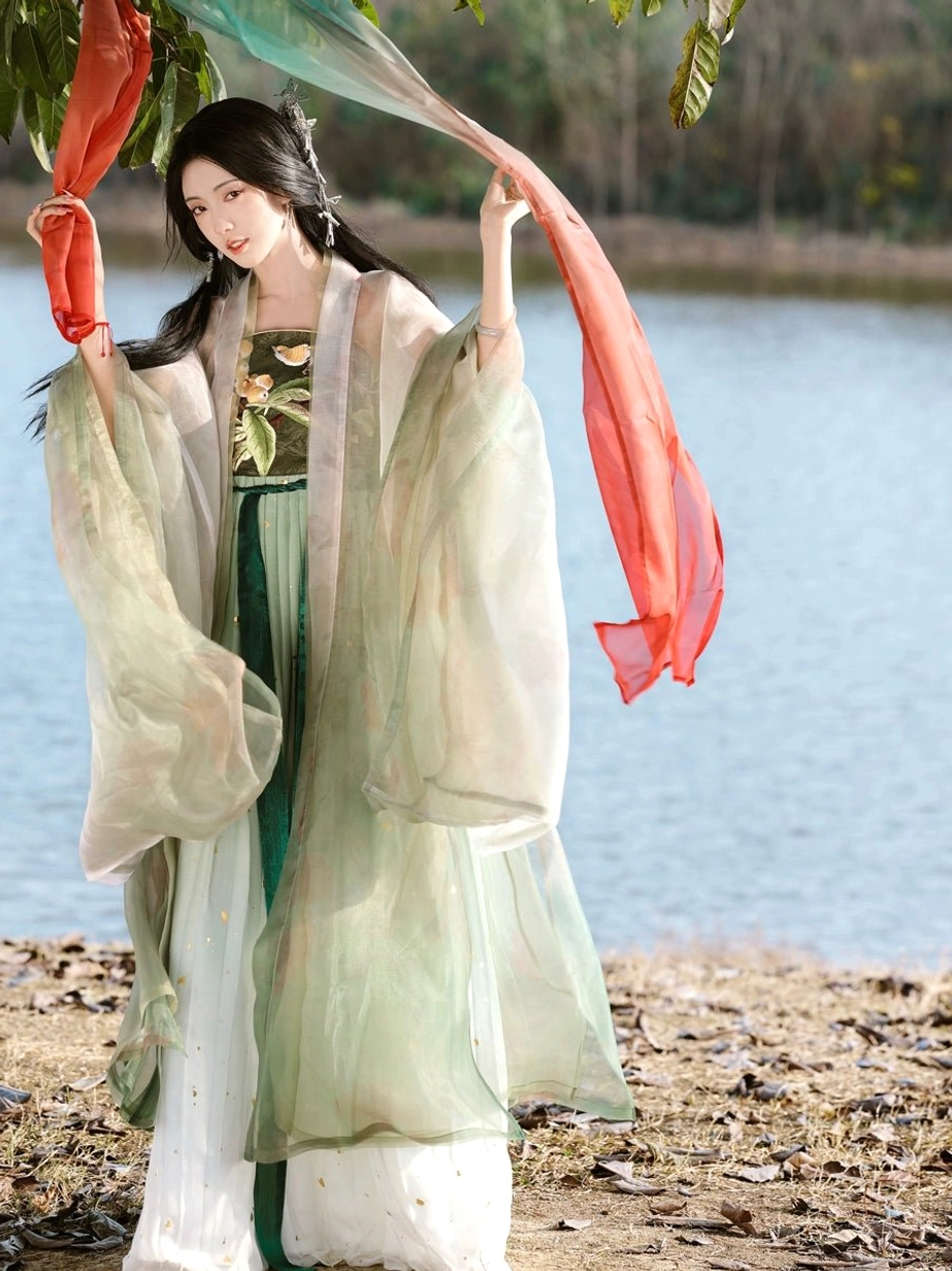 Pipa Beauty Tang Dynasty style Heziqun Hanfu dress in pale green with embroidered tube top, layered skirt, and sheer wide sleeve coat shown in a lakeside outdoor setting