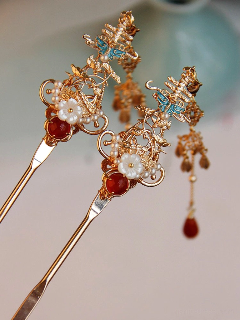 Vintage Chinese gold hair stick with red agate accent, white flower ornament, blue enamel butterfly and red tassel displayed on a light tabletop