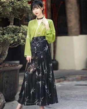 Pistachio green modern Hanfu three-piece set with cross-collar top yellow camisole and black bamboo-print horse-face skirt worn in an outdoor courtyard