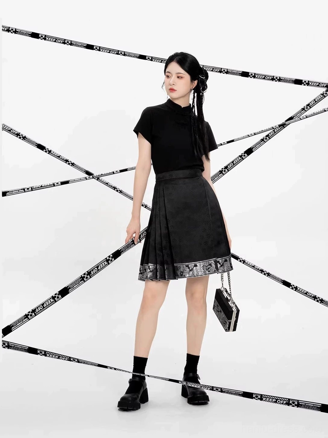 Front outfit view showing the pleated black mini mamian skirt and traditional-inspired patterned hem with monochrome accessories